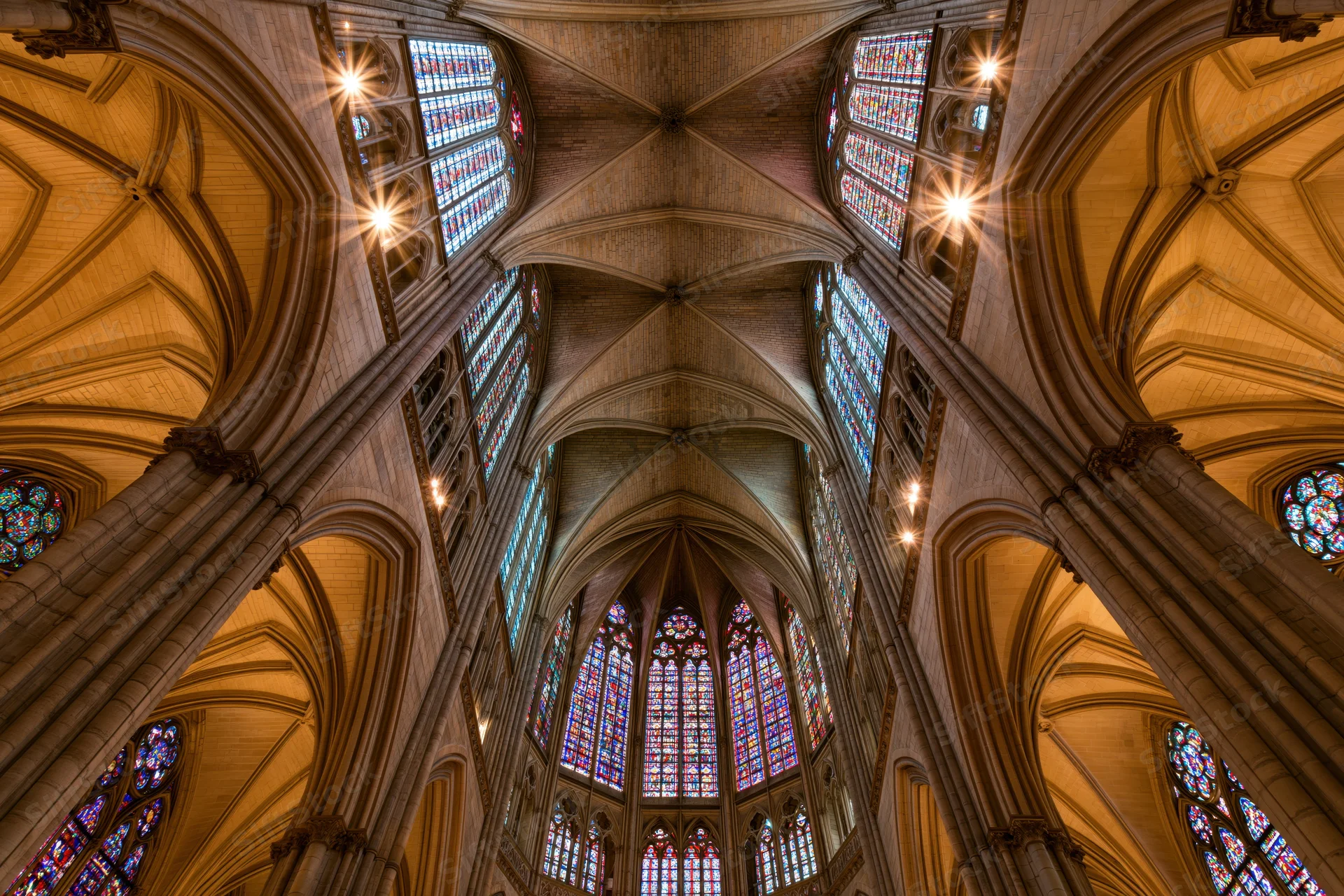 Upward view of gothic cathedral nave with vaulted stone ceiling and stained glass windows