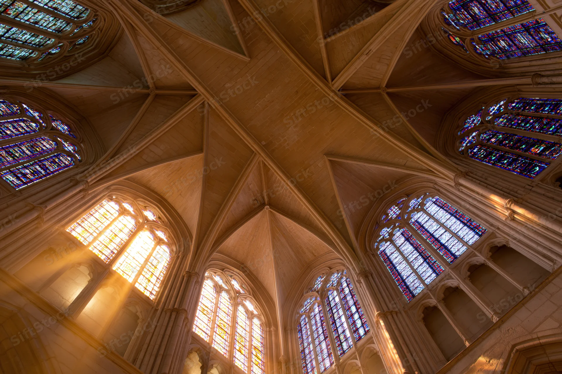 Upward view of a gothic cathedral nave ceiling with ribbed vaults and stained glass windows