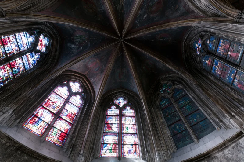 Upward view of a gothic church apse with vaulted stone ceiling and stained glass windows
