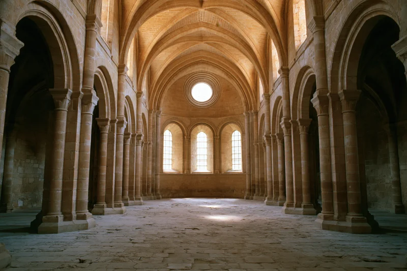 Interior of a roman church nave with stone arches and vaulted ceiling leading to apse windows