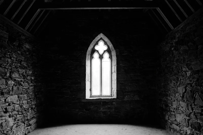 Dark interior of a medieval stone chapel with a single tall gothic window letting in light
