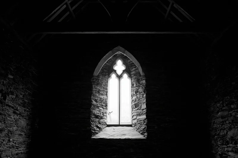 Dark interior of a medieval stone chapel with a single tall gothic window letting in light
