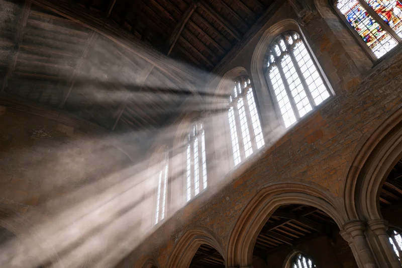Sunlight beams through stained glass windows in the stone nave of a medieval english cathedral