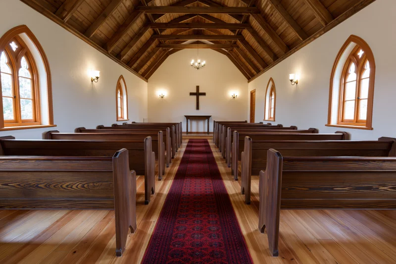 Empty wooden pews lining a red carpeted aisle in a small historic chapel interior