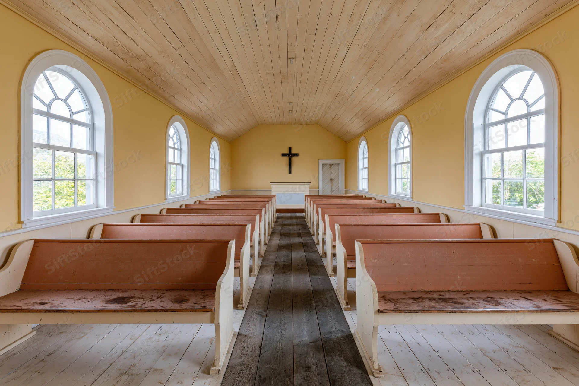 Empty wooden pews arranged in rows inside a small historic church with yellow walls and arched windows