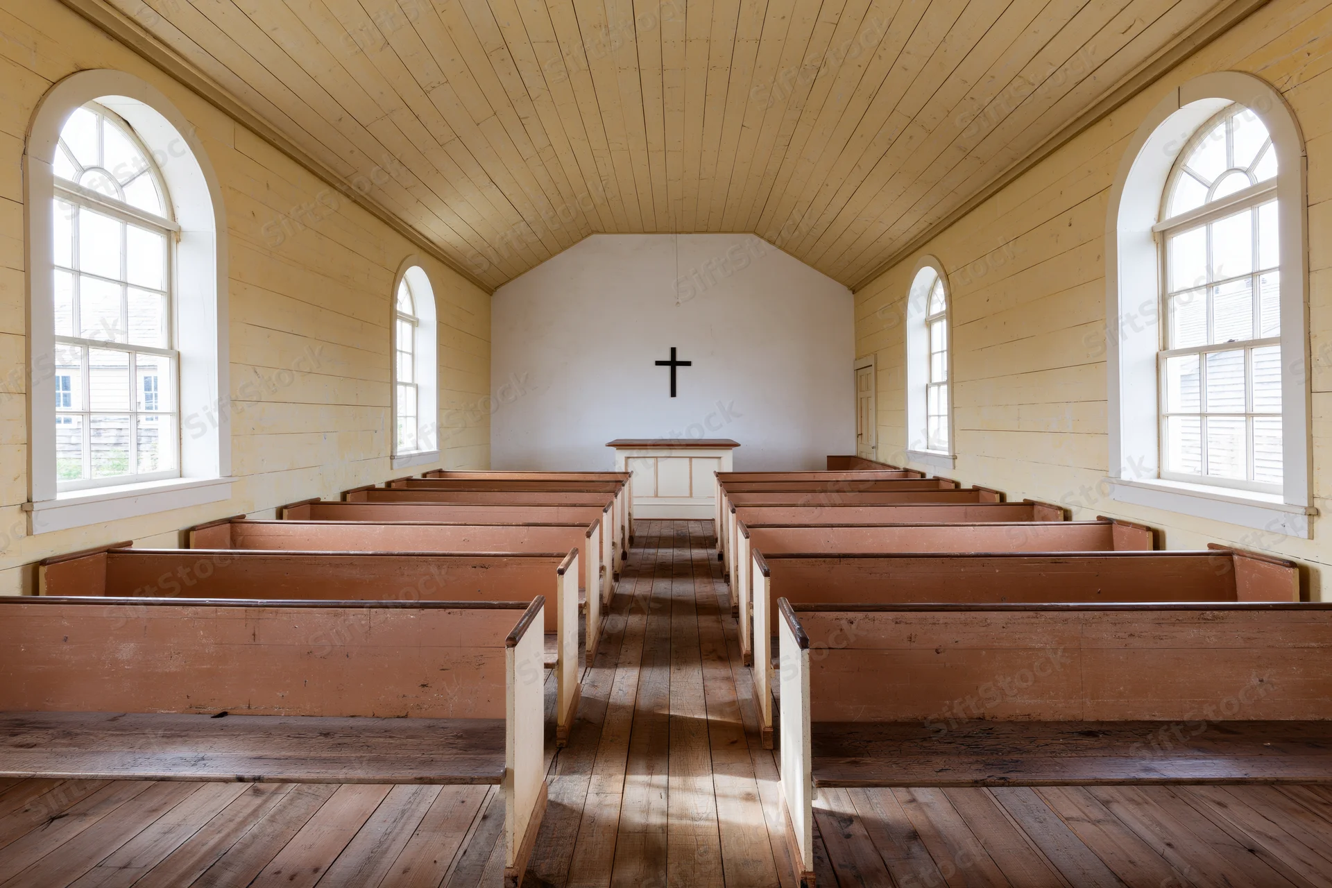 Empty wooden pews receding toward a cross at the front of a small historic church interior