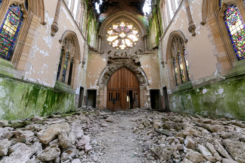 Interior of abandoned gothic church nave with collapsed ceiling and rubble covering floor, stained glass windows intact