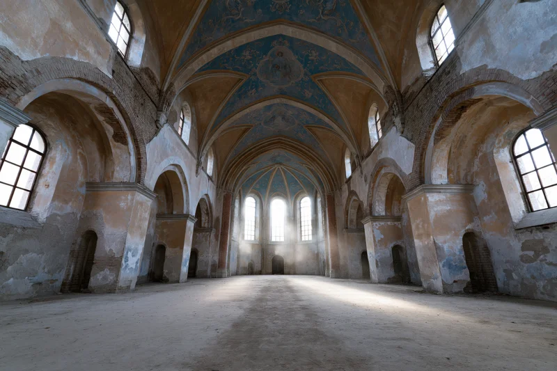 Empty nave of an abandoned roman church with vaulted ceiling and arched windows