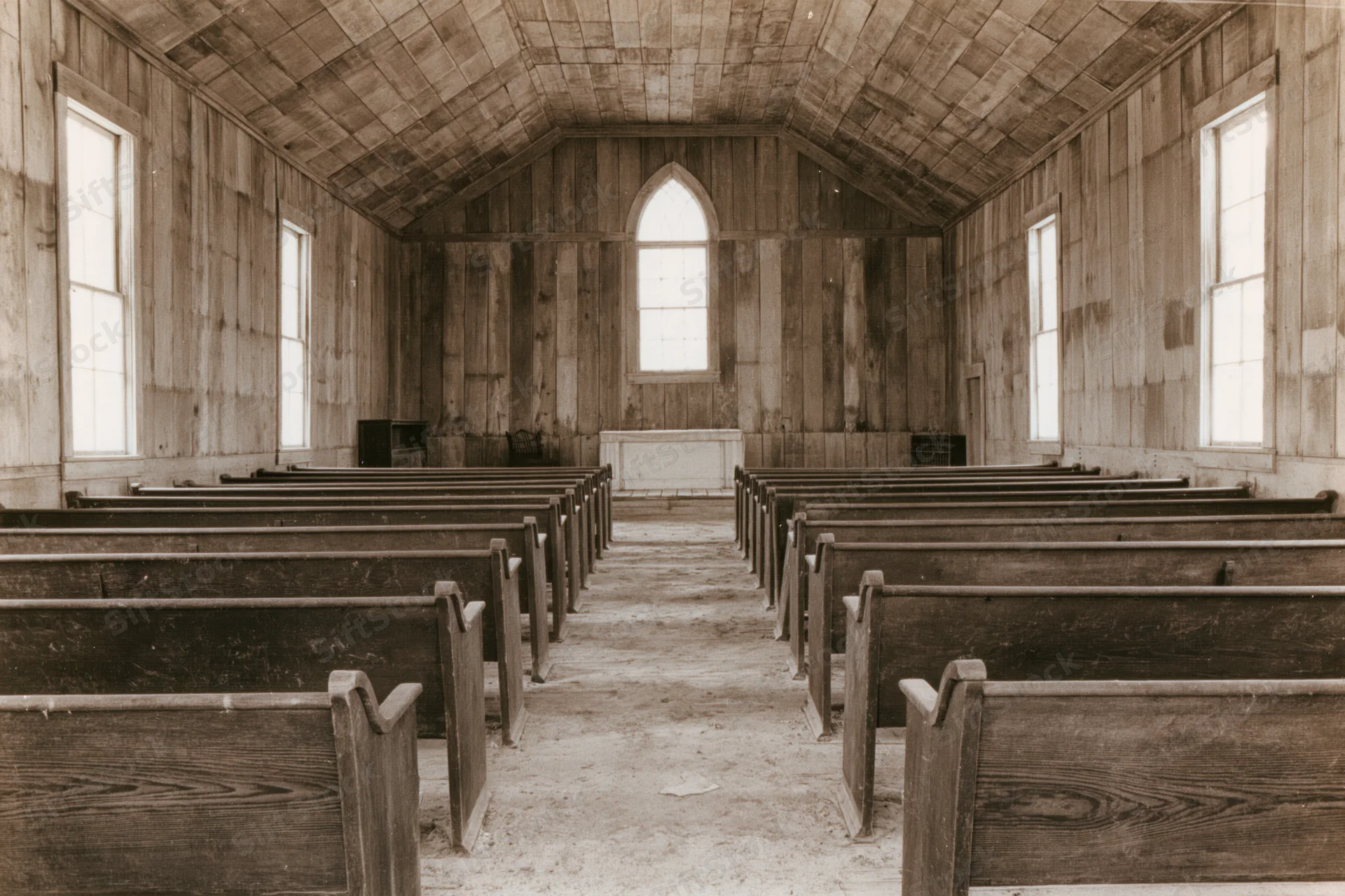 Interior of an abandoned rural wooden church with rows of pews and arched windows