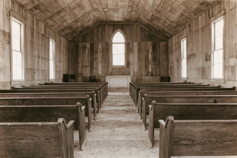 Interior of an abandoned rural wooden church with rows of pews and arched windows