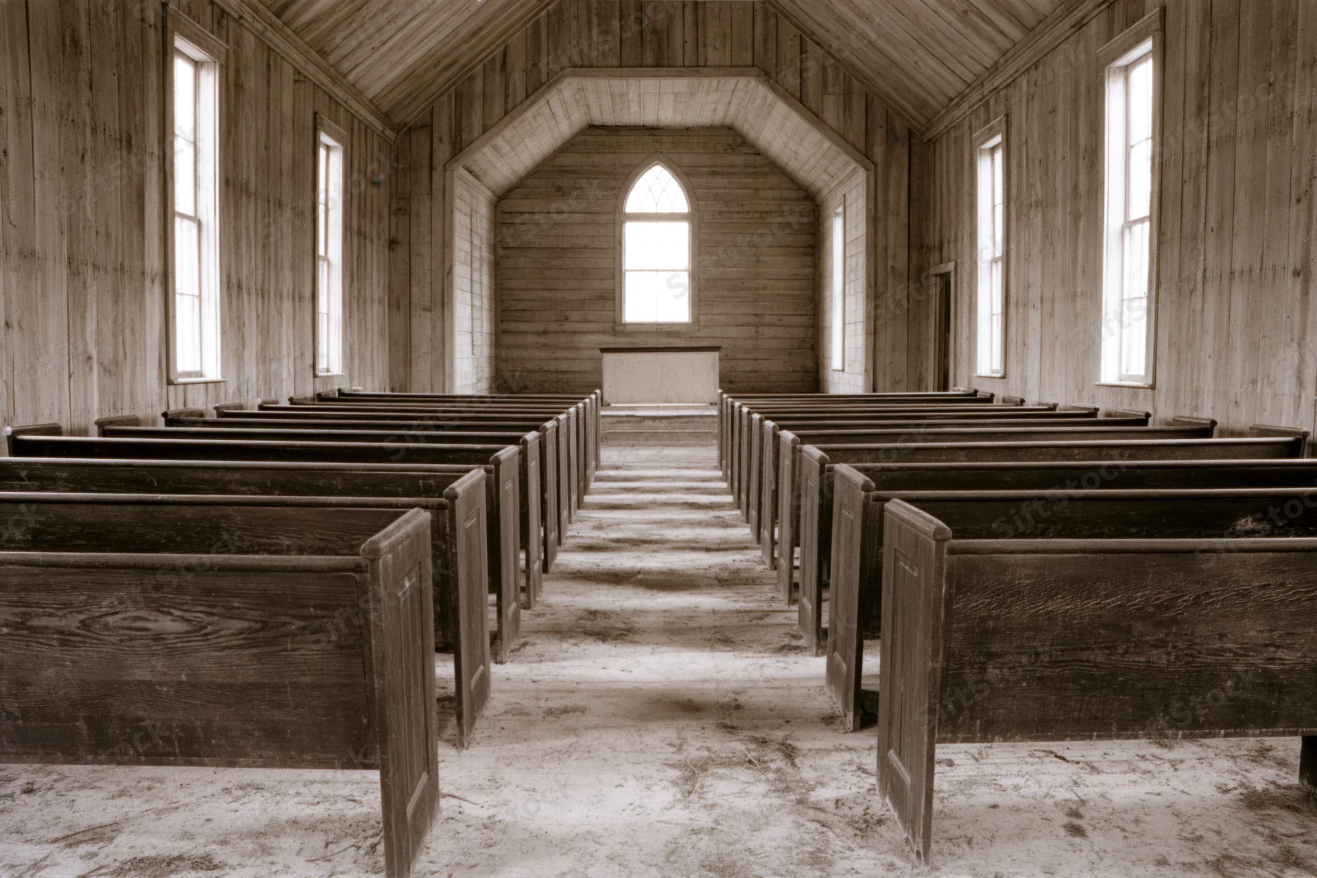 Empty wooden pews in a rural abandoned church interior with arched windows and dirt floor