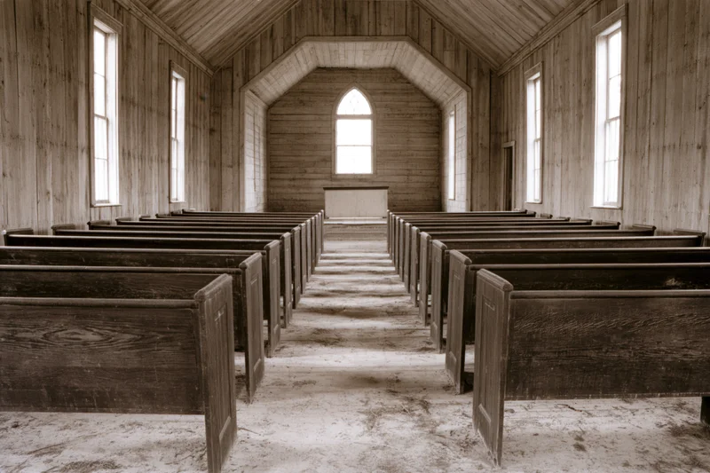 Empty wooden pews in a rural abandoned church interior with arched windows and dirt floor