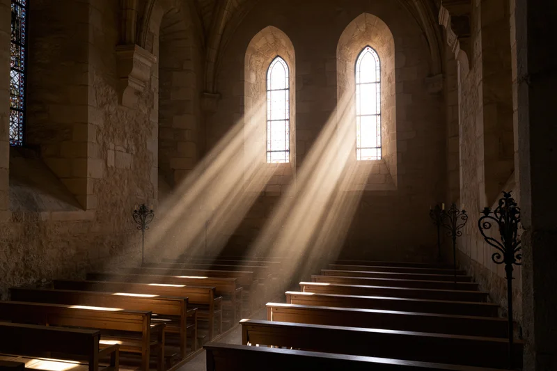 Sunlight streaming through arched windows onto wooden pews in an old stone church interior