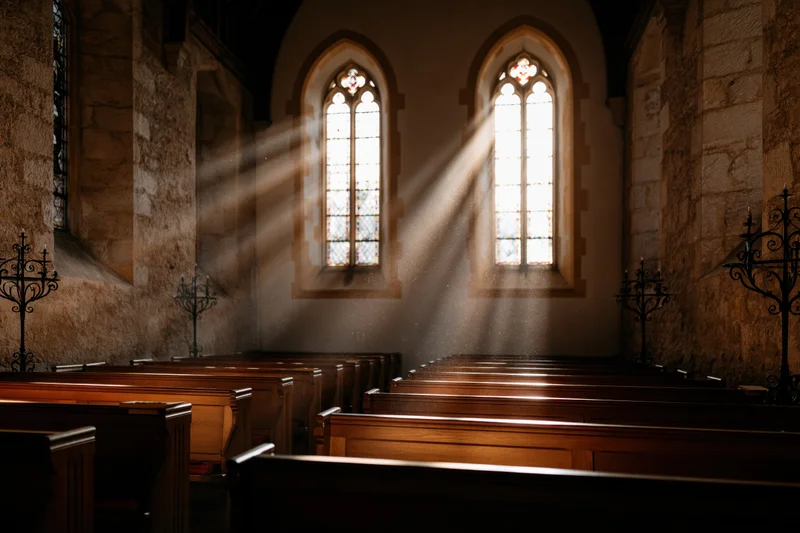 Sunlight streaming through arched stained glass windows in an old stone church interior with wooden pews receding into shadow