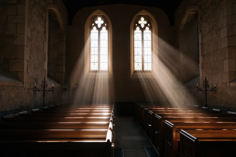 Sunlight streaming through arched stained glass windows onto wooden pews in an empty stone church interior