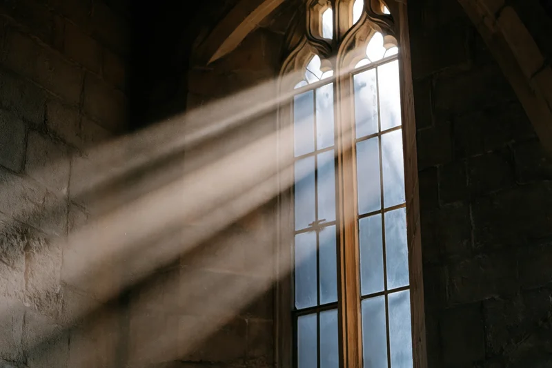 Sunlight streaming through a tall gothic arched window in an old stone church interior