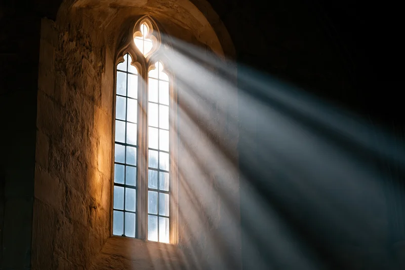 Sunlight streaming through a tall gothic arched window in an old stone church interior