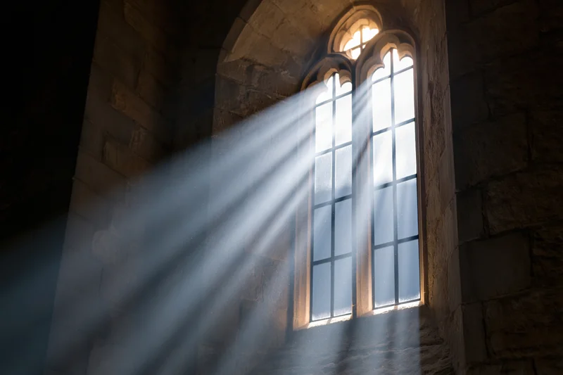 Sunlight streaming through a tall gothic arched window in an old stone church interior