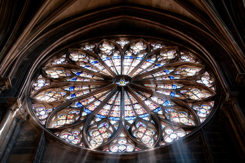 Upward view of a gothic cathedral rose window with stained glass and sunlight streaming through