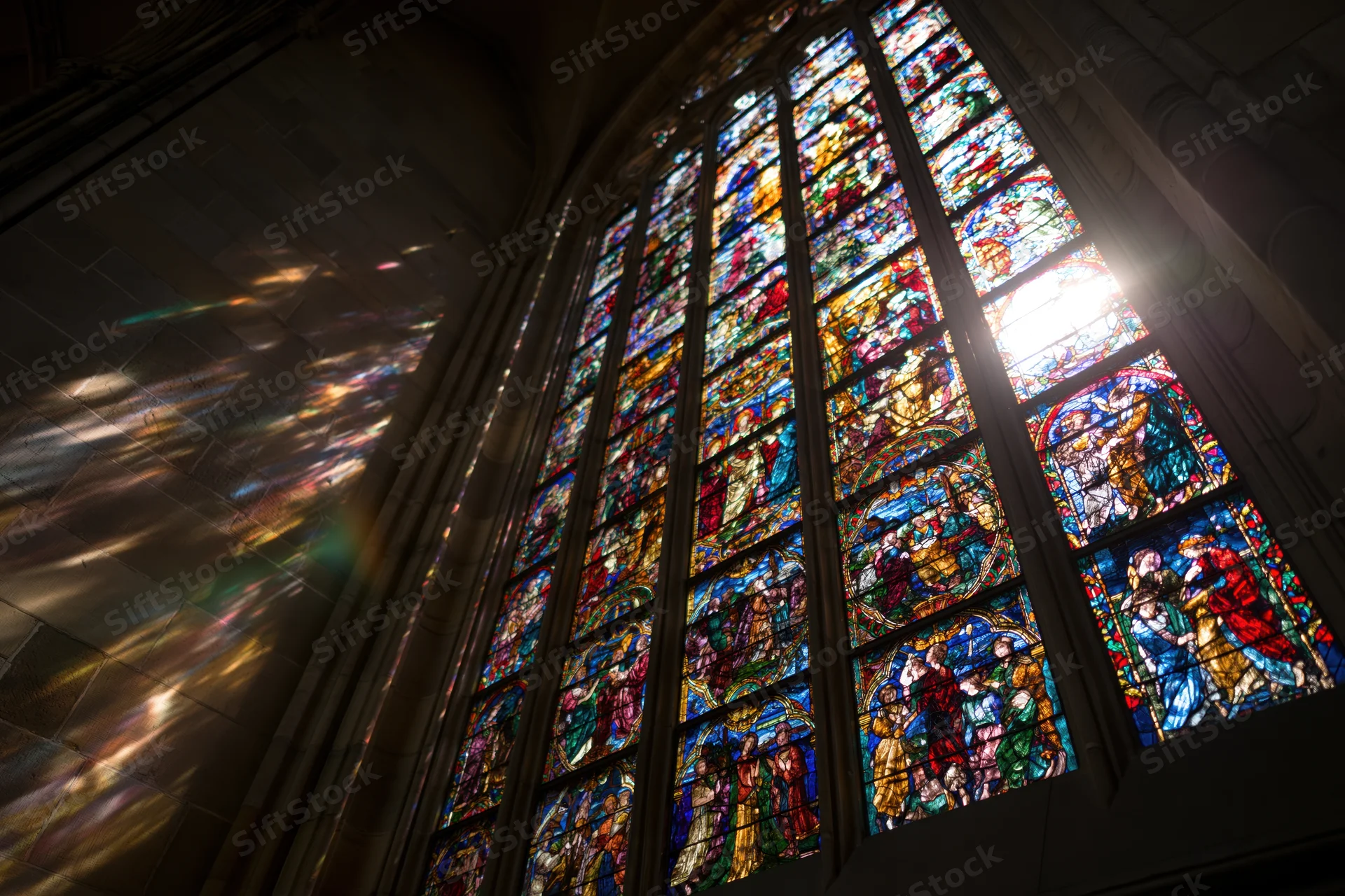 Large gothic stained glass window in cathedral interior glowing with backlit light