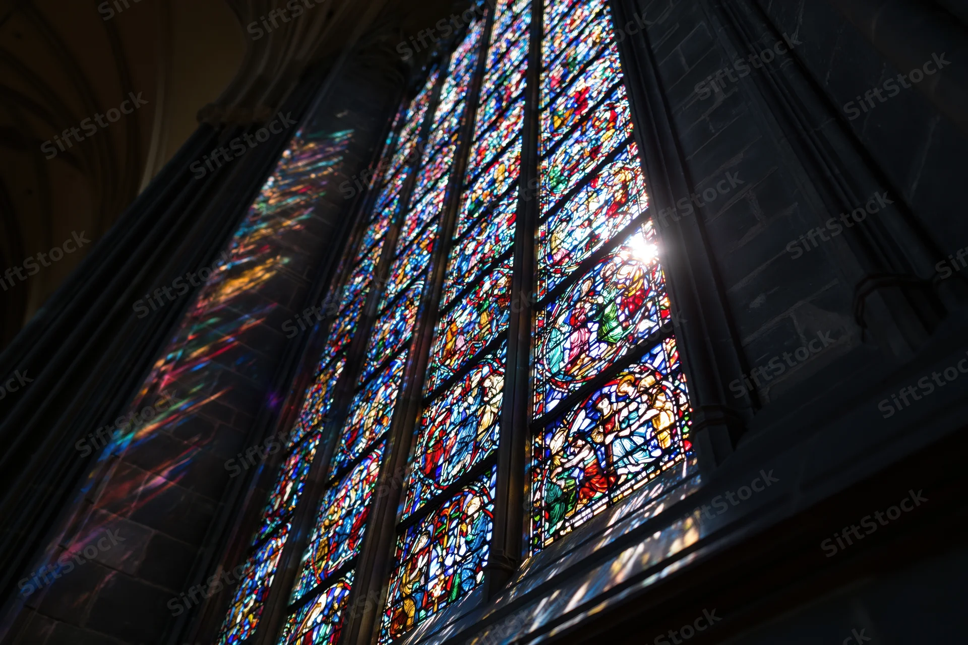 Large gothic stained glass window glowing with sunlight in cathedral interior
