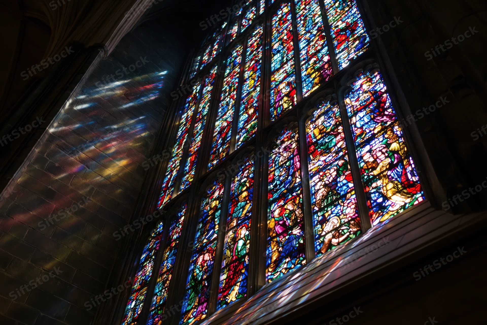 Large gothic stained glass window glowing with light inside a cathedral interior