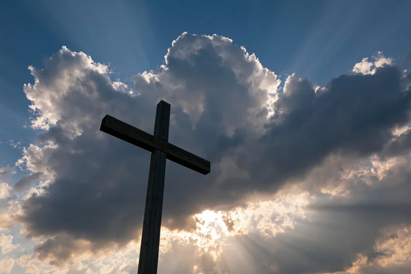 Wooden christian cross silhouetted against dramatic sky with sun rays through clouds