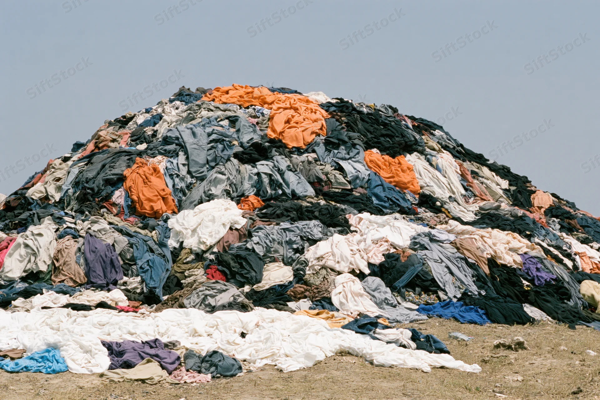 Massive mound of discarded clothing piled high outdoors on dry ground