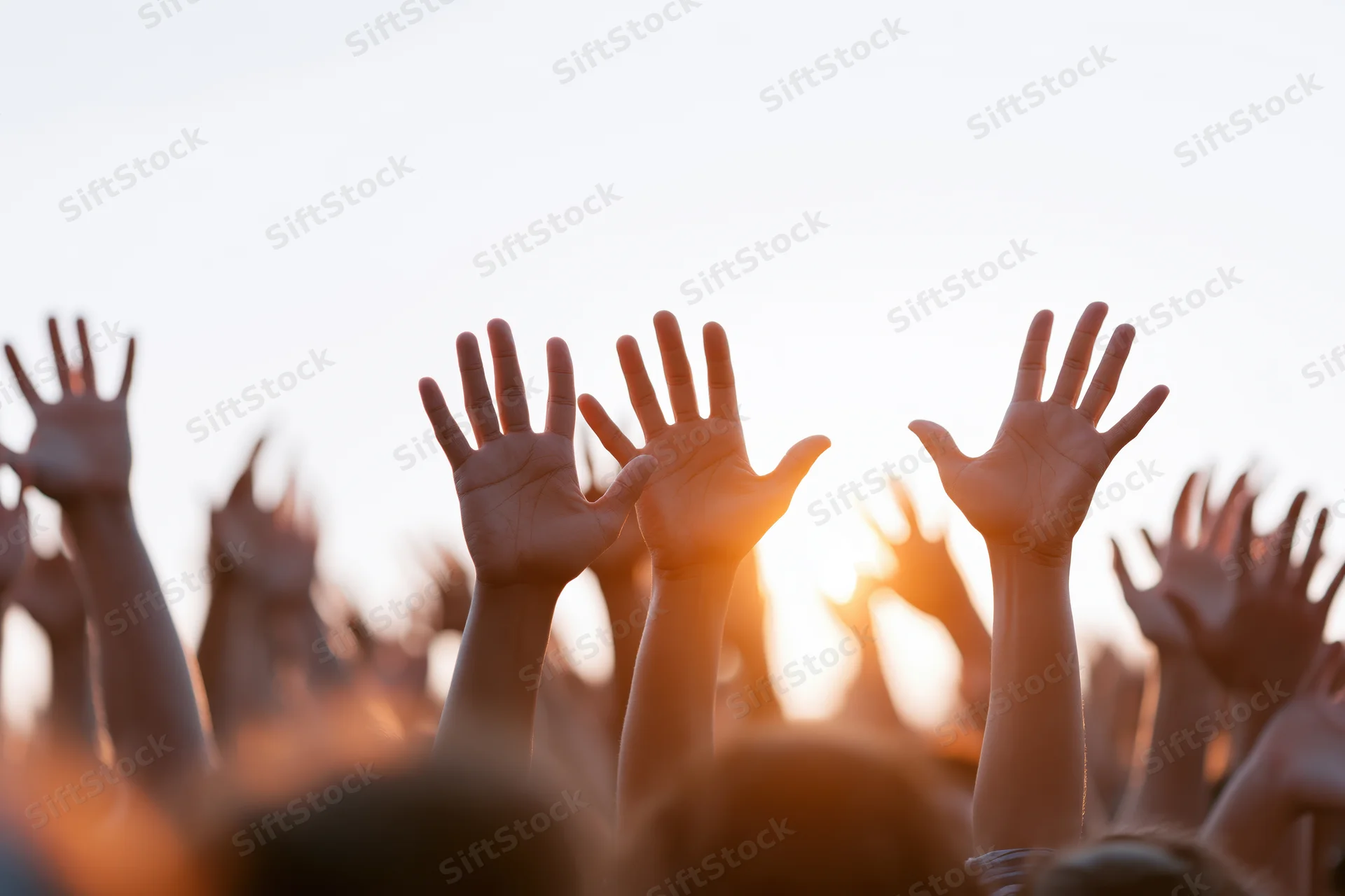 Multiple hands raised upward from a crowd at sunset during an outdoor event