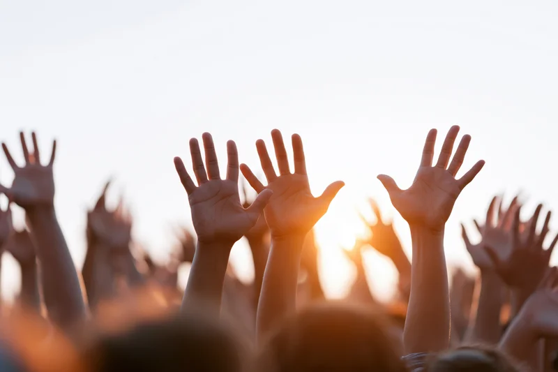 Multiple hands raised upward from a crowd at sunset during an outdoor event