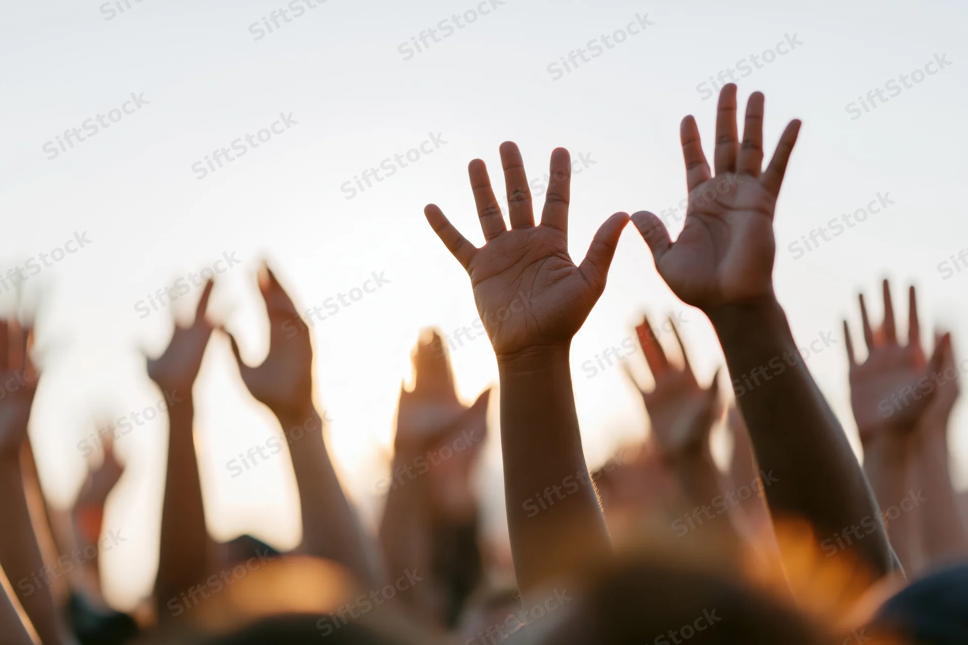 Multiple hands raised upward from a crowd at sunset during an outdoor event