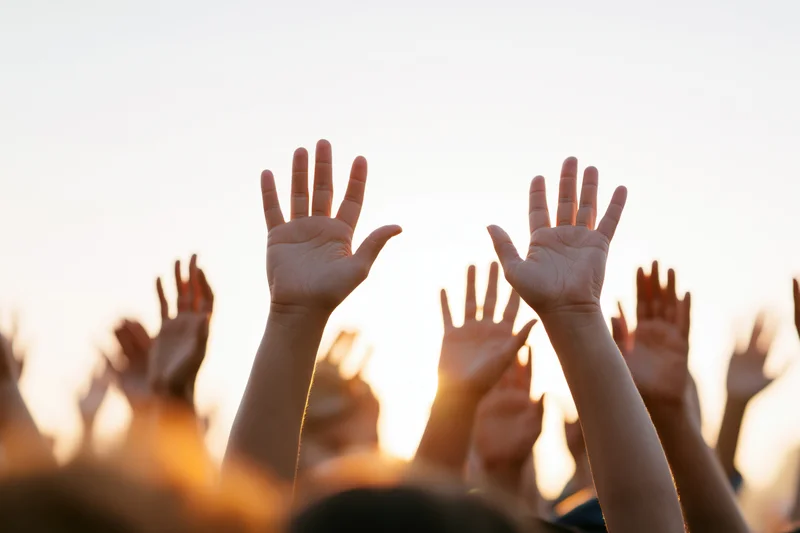 Multiple hands raised upward from a crowd at sunset outdoors