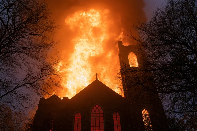 Gothic stone church engulfed in flames at night with cross and tower silhouetted against fire and smoke