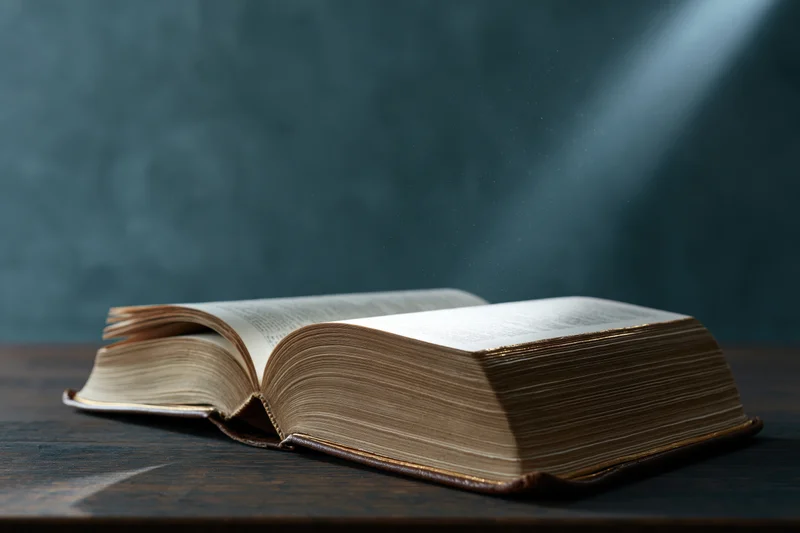 Open hardcover bible with gilded page edges lying flat on wooden table under focused light beam