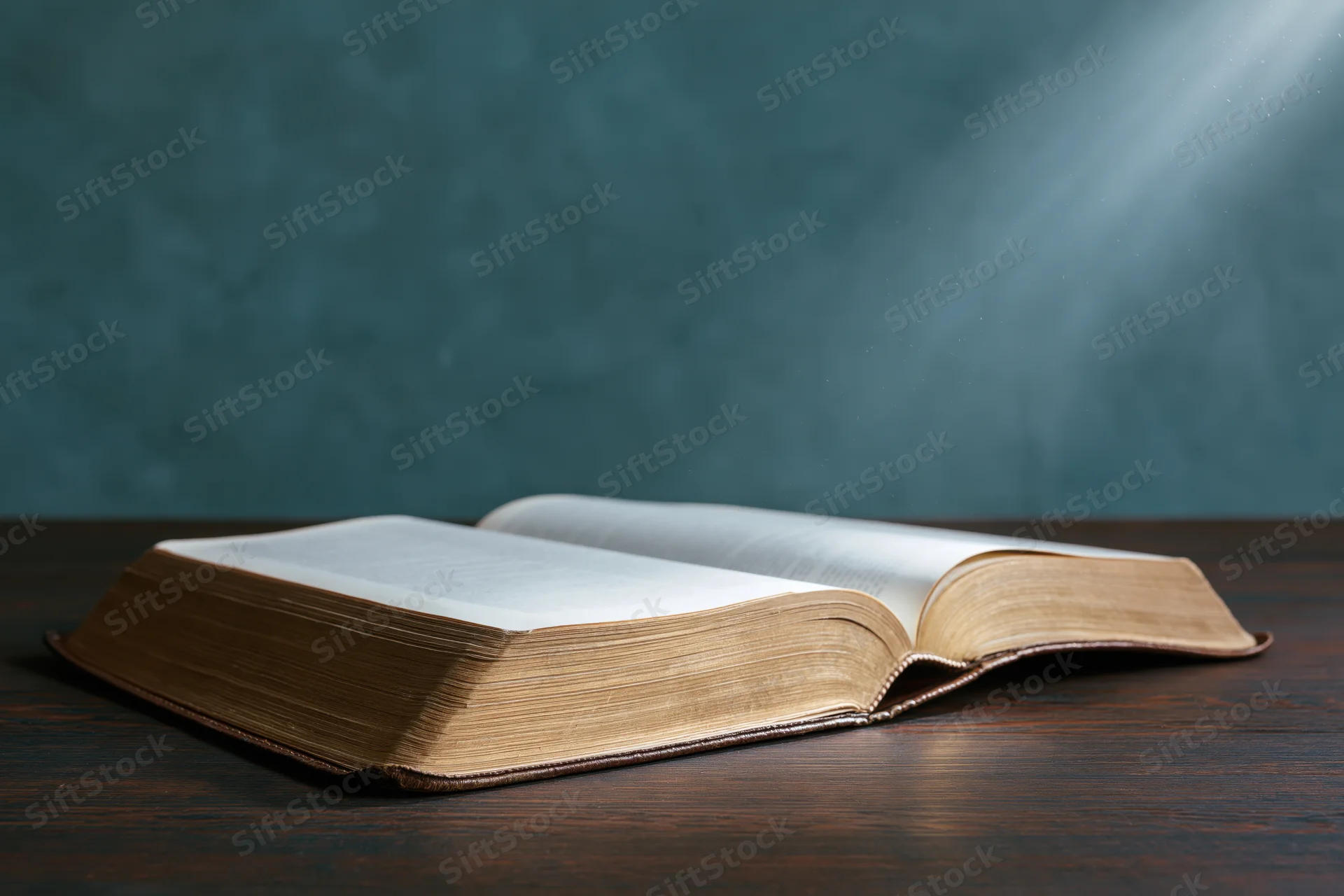 Open bible lying flat on wooden surface with light beam from above
