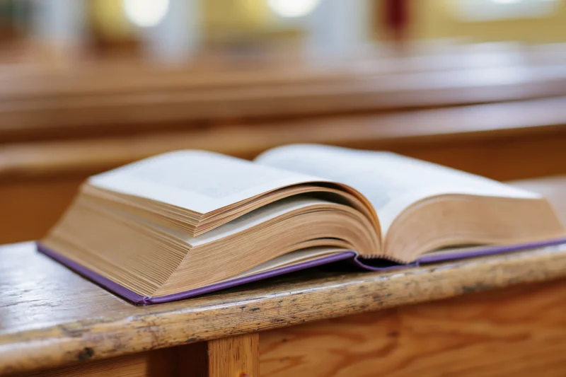 Open hardcover bible resting on wooden church pew with shallow depth of field