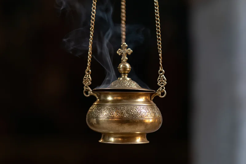 Ornate brass censer hanging with smoke rising from it in a church setting