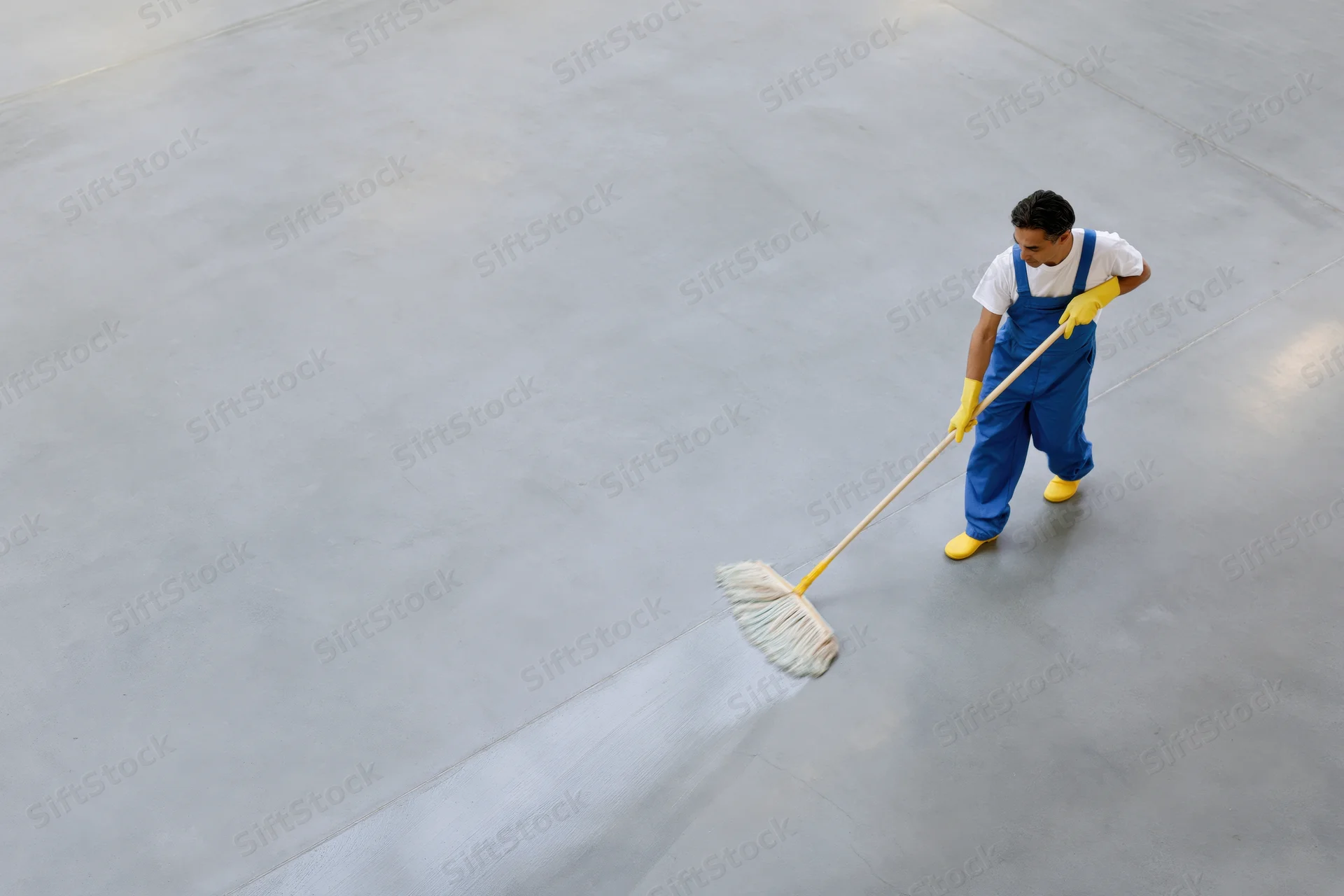Male janitor mopping large concrete floor from overhead view