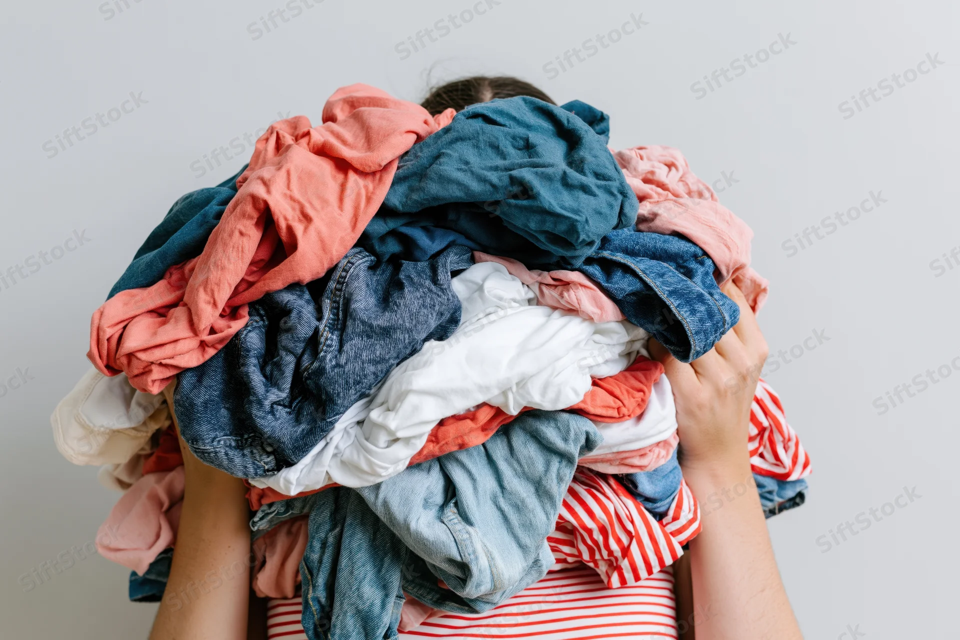 Woman holding large pile of laundry over her head in a white room