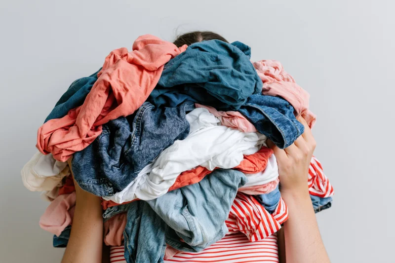 Woman holding large pile of laundry over her head in a white room