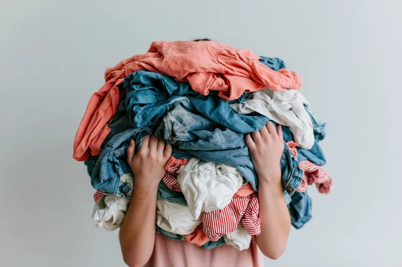 Woman holding large pile of laundry covering her face in a plain indoor setting