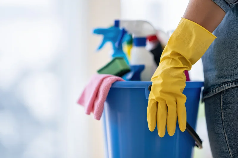 Woman holding a blue bucket filled with cleaning supplies in a home interior