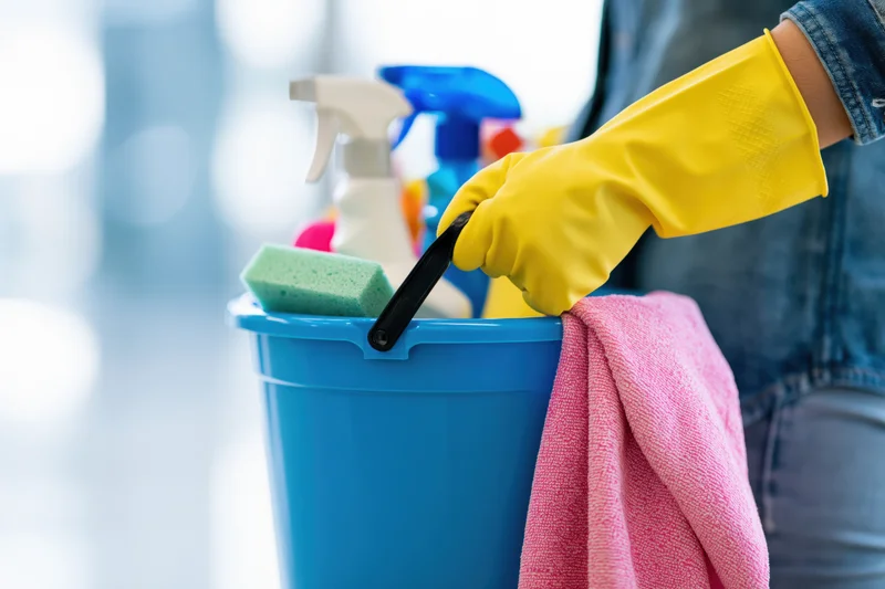 Woman holding a blue bucket filled with cleaning supplies and wearing yellow gloves