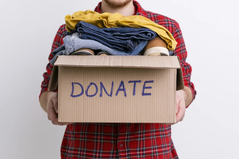 Man holding cardboard box labeled donate filled with folded clothes and shoes