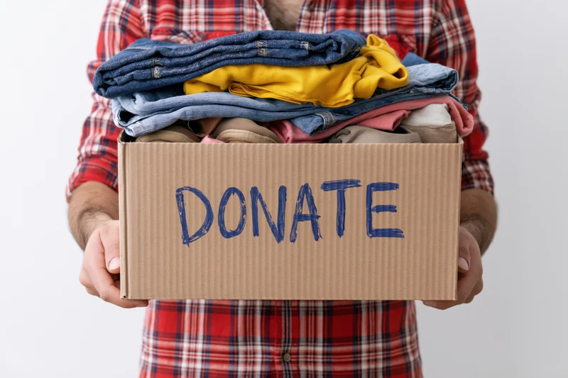 Man holding a cardboard box labeled donate filled with folded clothes