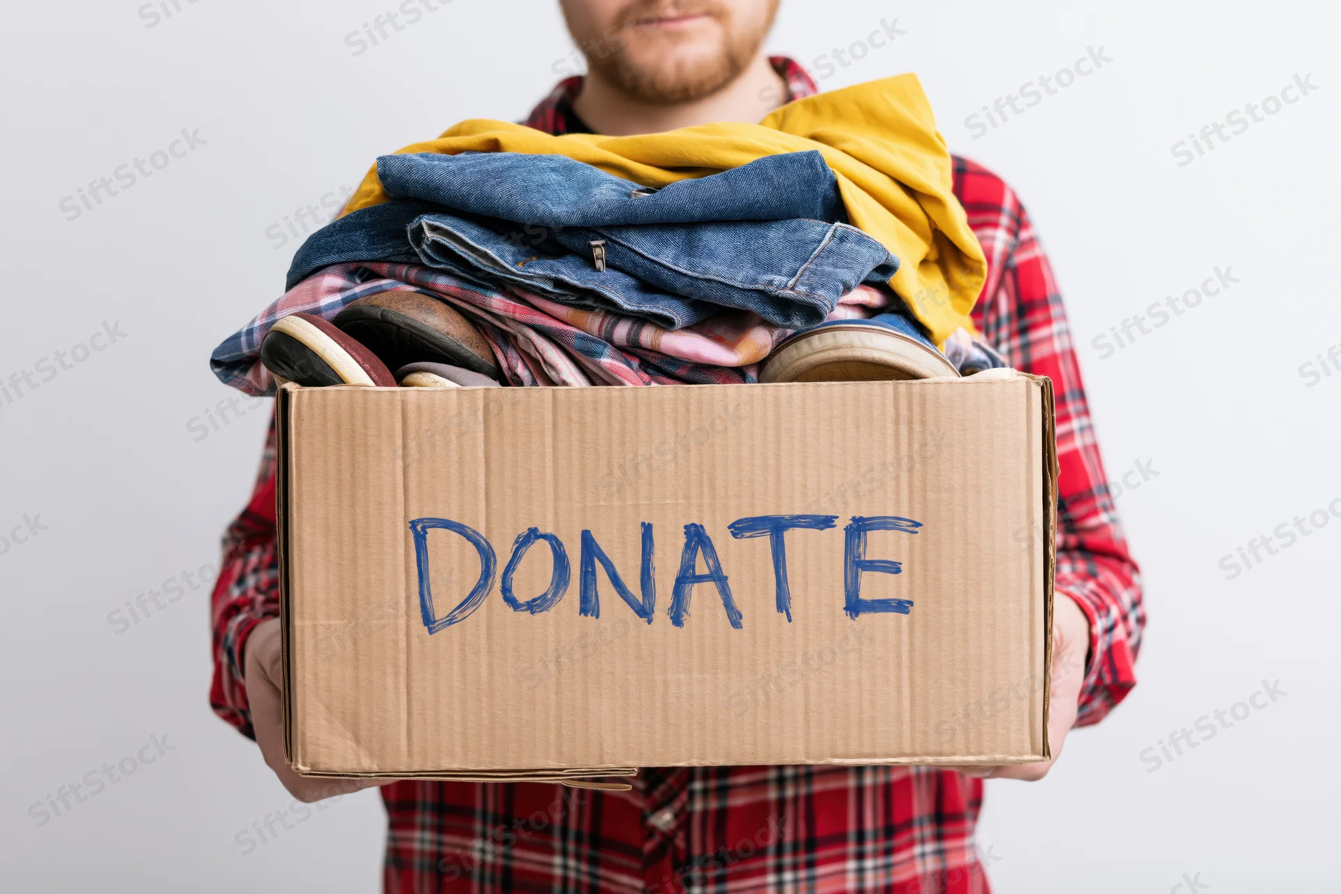 Man holding cardboard box labeled donate filled with folded clothes and shoes