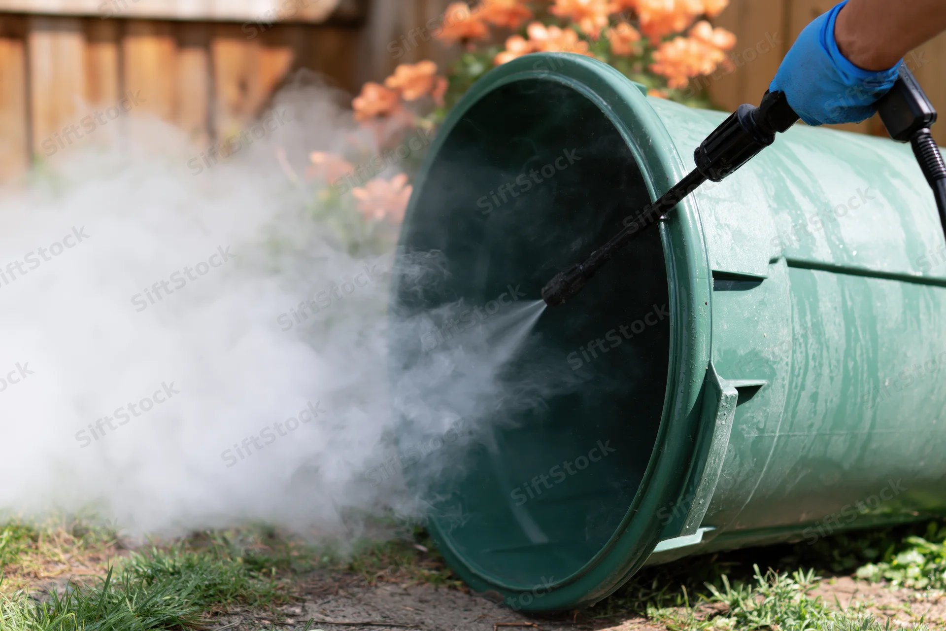 Person pressure washing inside of large green plastic compost bin in backyard garden