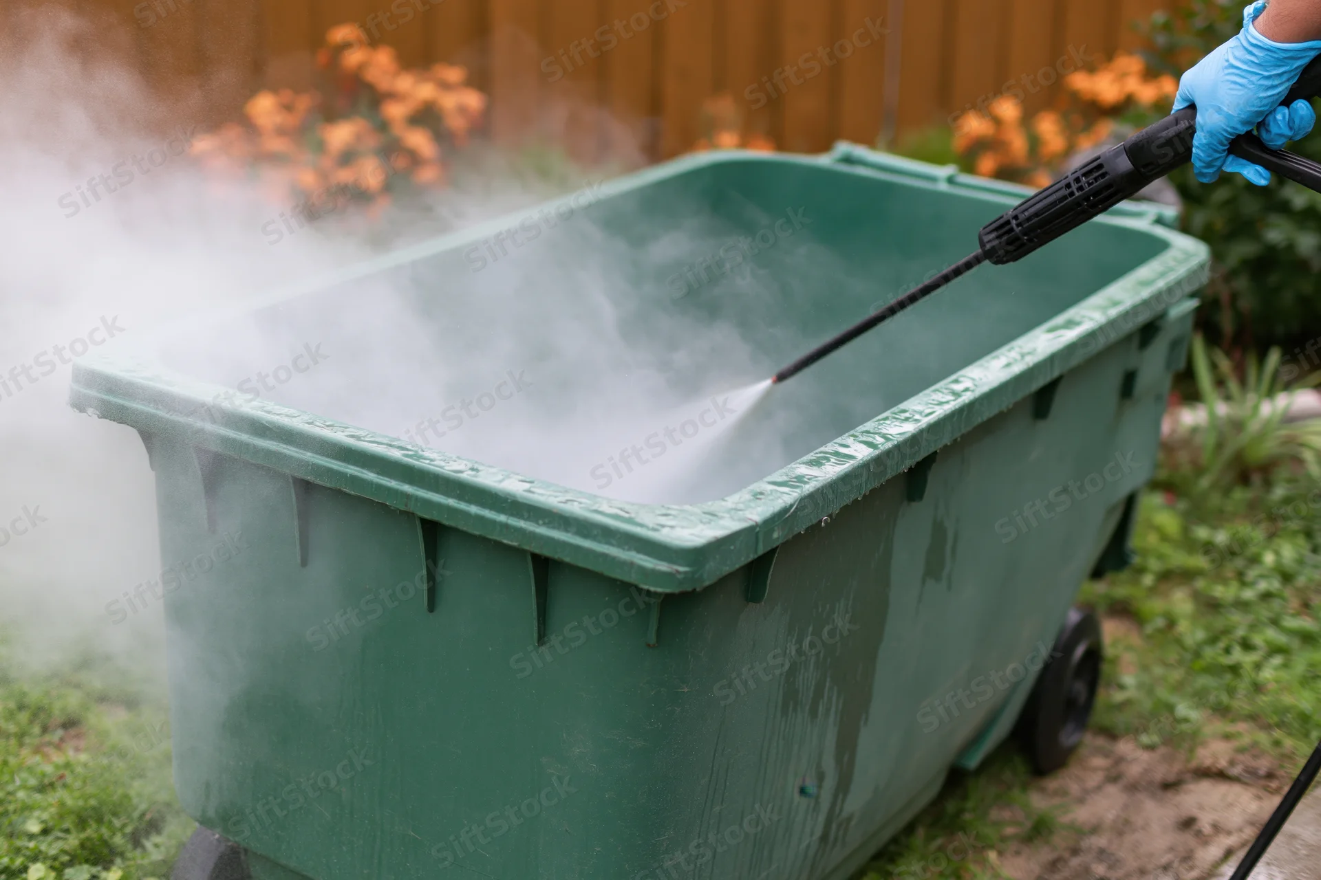 Person pressure washing inside of large green plastic trashcan in garden
