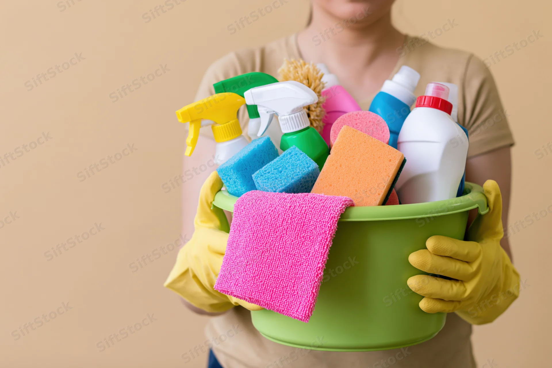 Woman holding a green bucket filled with cleaning supplies and wearing yellow gloves