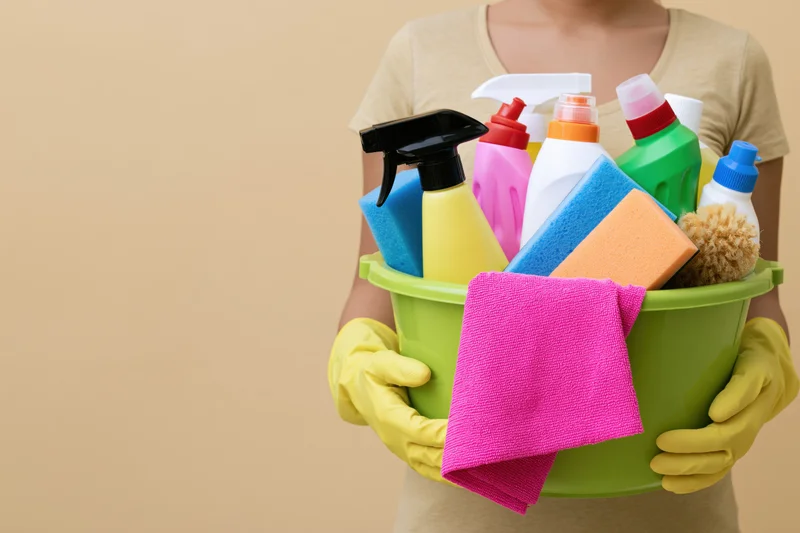 Woman holding a green bucket filled with cleaning supplies and wearing yellow gloves